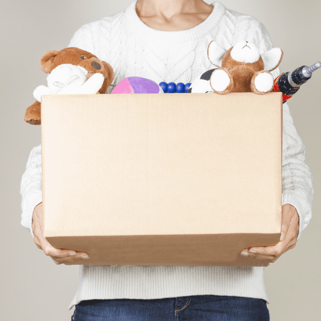 woman holding a cardboard box of children's stuffed animals and toys