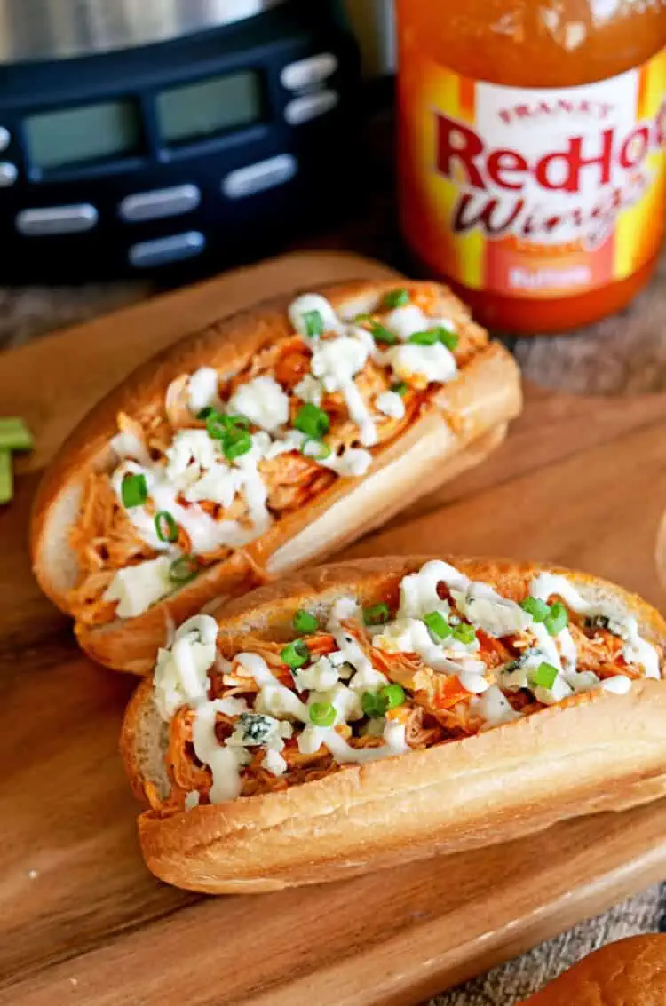 Slow cooker shredded buffalo chicken sandwitches sprinkled with ranch sauce and green onion
