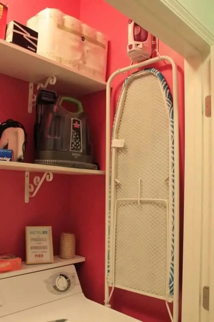 DIY ironing station hanged on a wall with an iron on top in a tiny laundry room with red walls and white shelve