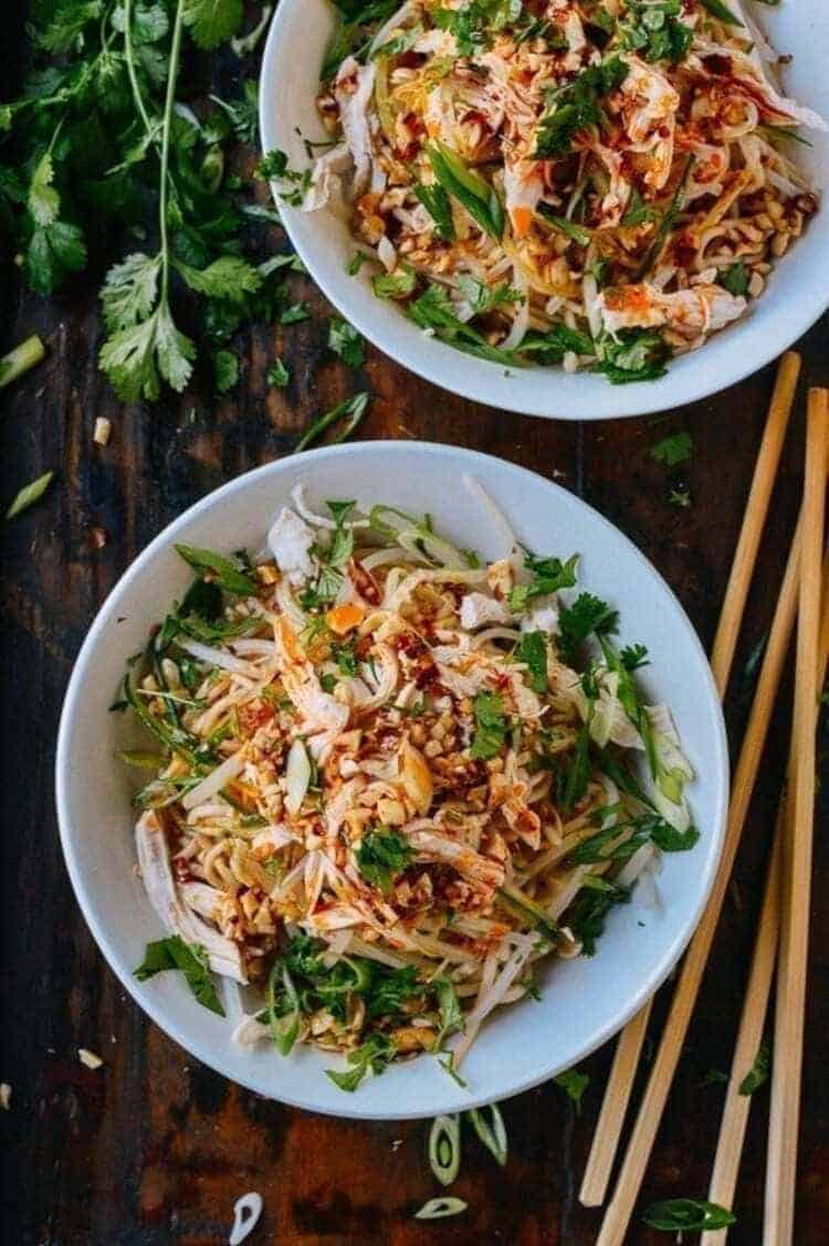 cold noodles with shredded chicken, two white plates on a dark table, sprinkled with parsley