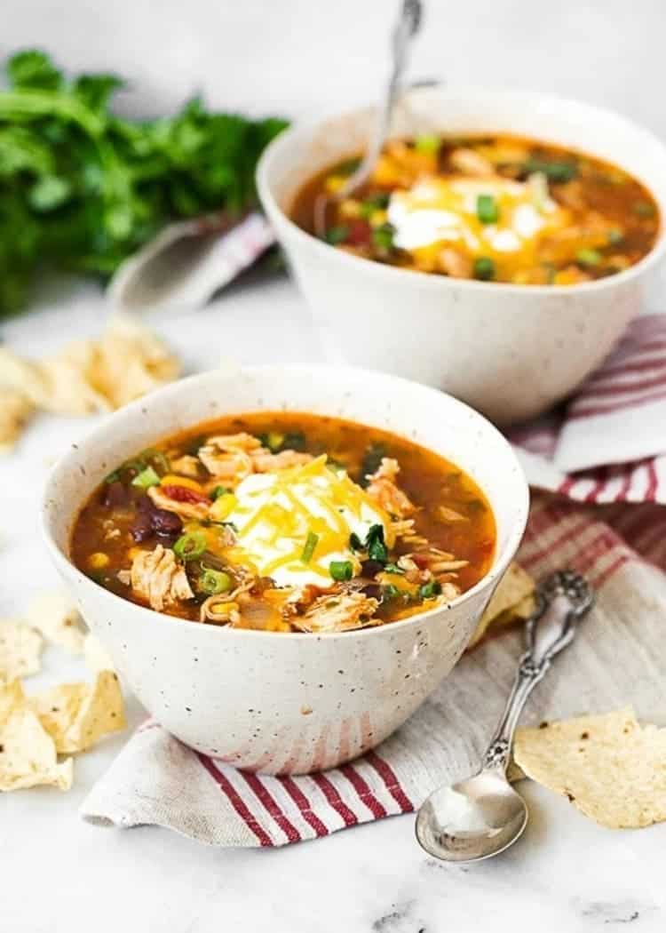 Chicken Enchilada Soup two white bowls with sour cream with green onion and parsley