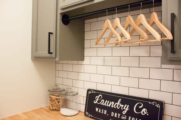 small laundry room with green wall cabinets with a rod between them with clothes hangers on it