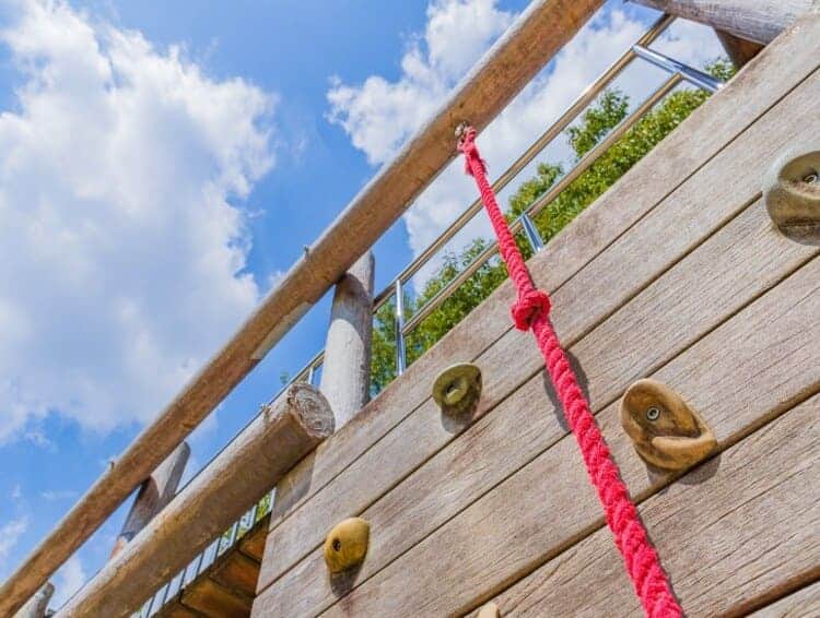 outside backyard playset wit wooden climbing wall and a red rope