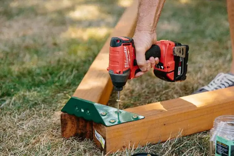 man assembling wooden playset with metal joints, brown and dark green on the grass