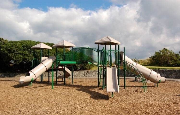 backyard playset with swing set, three wooden towers and four slides, wooden and metal with dark green and brown color, on a green landscape