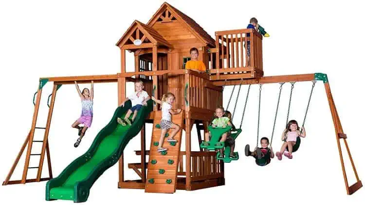 Large wooden playset with swings, slide, monkey bars, climbing wall, a wooden roof,upper porch, bay windows, snack stand, piccnic table, sandbox and a sun deck