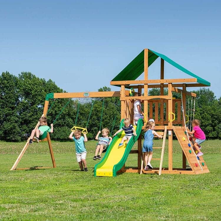 Wooden playset with double rock wall and a rope, swing beam with heavy duty steel brackets, wave slide and upper fort, brown and green on a green landscape