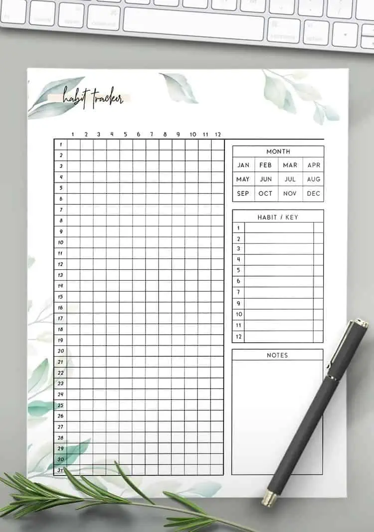 monthly yearly habit tracker printable with leafs on letterhead on a grey table with a pen on it