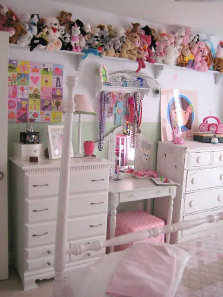 stuffed animal storage on a long wall shelf full of stuffed toys in a girls room with white furniture