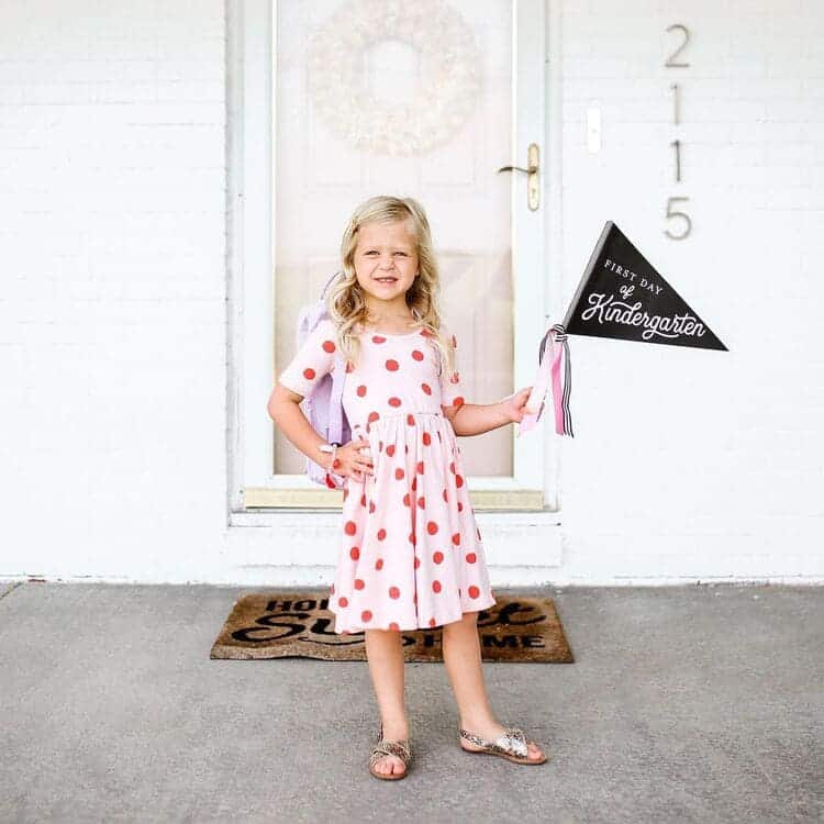 blond girl with a polka dot dress holding a first day of school flag