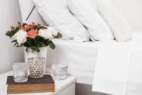 small vase of flowers and cup of water on nightstand next to bed