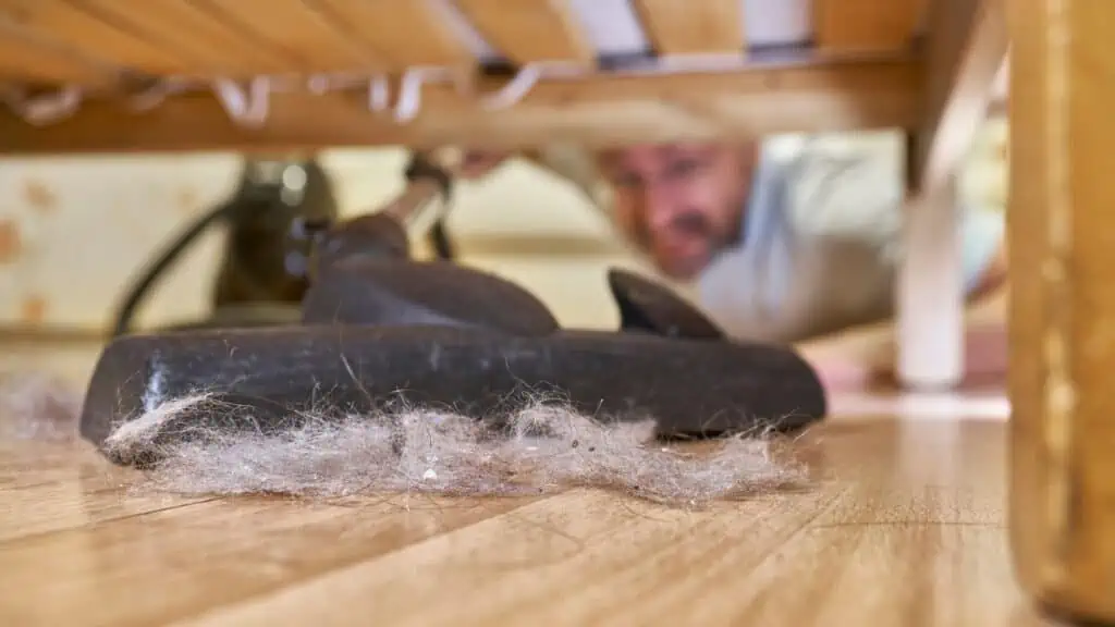 man vacuuming dust bunny under bed