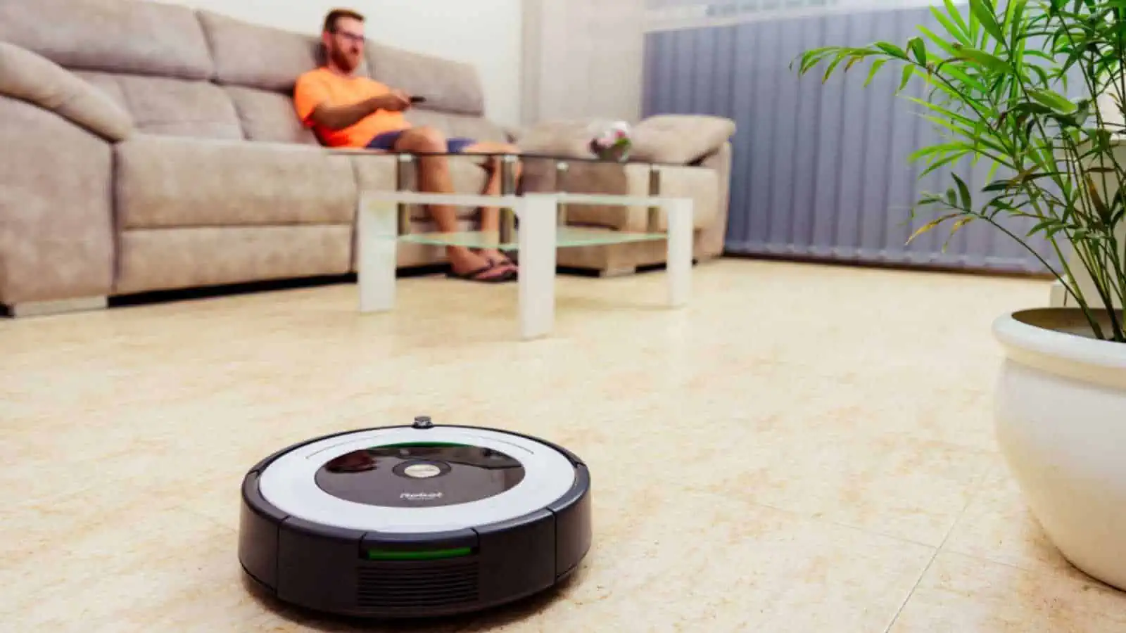 Berlin, Germany, August 29, 2019. Man sitting on a sofa watching TV while the irobot roomba cleans the living room floor. Moment relaxation.