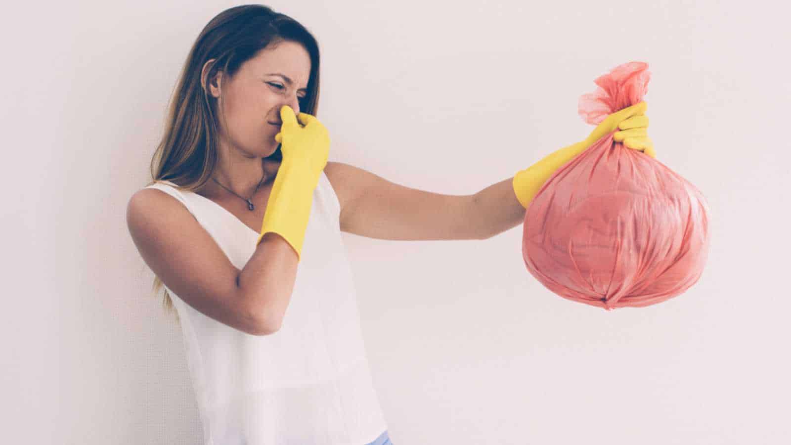 Unhappy woman holding trash with disgusting smell and holding nose to not feeling scent. Emotional young woman taking out trash. Garbage concept