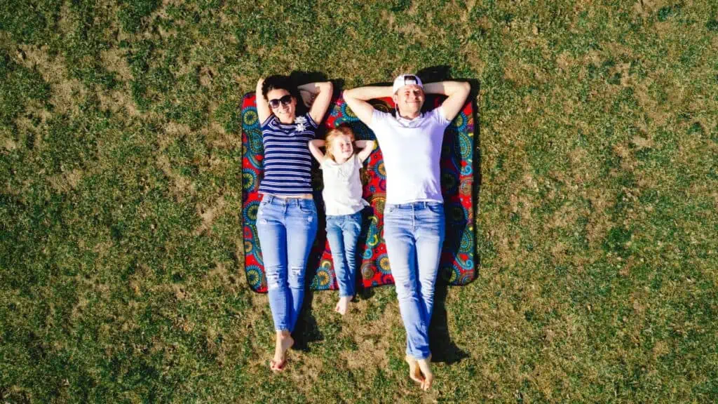 two adults and one small child lying on blanket and grass on a sunny day