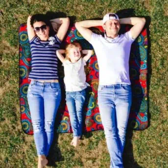 two adults and one small child lying on blanket and grass on a sunny day