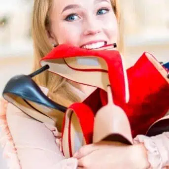 woman carrying shoes with one in her mouth
