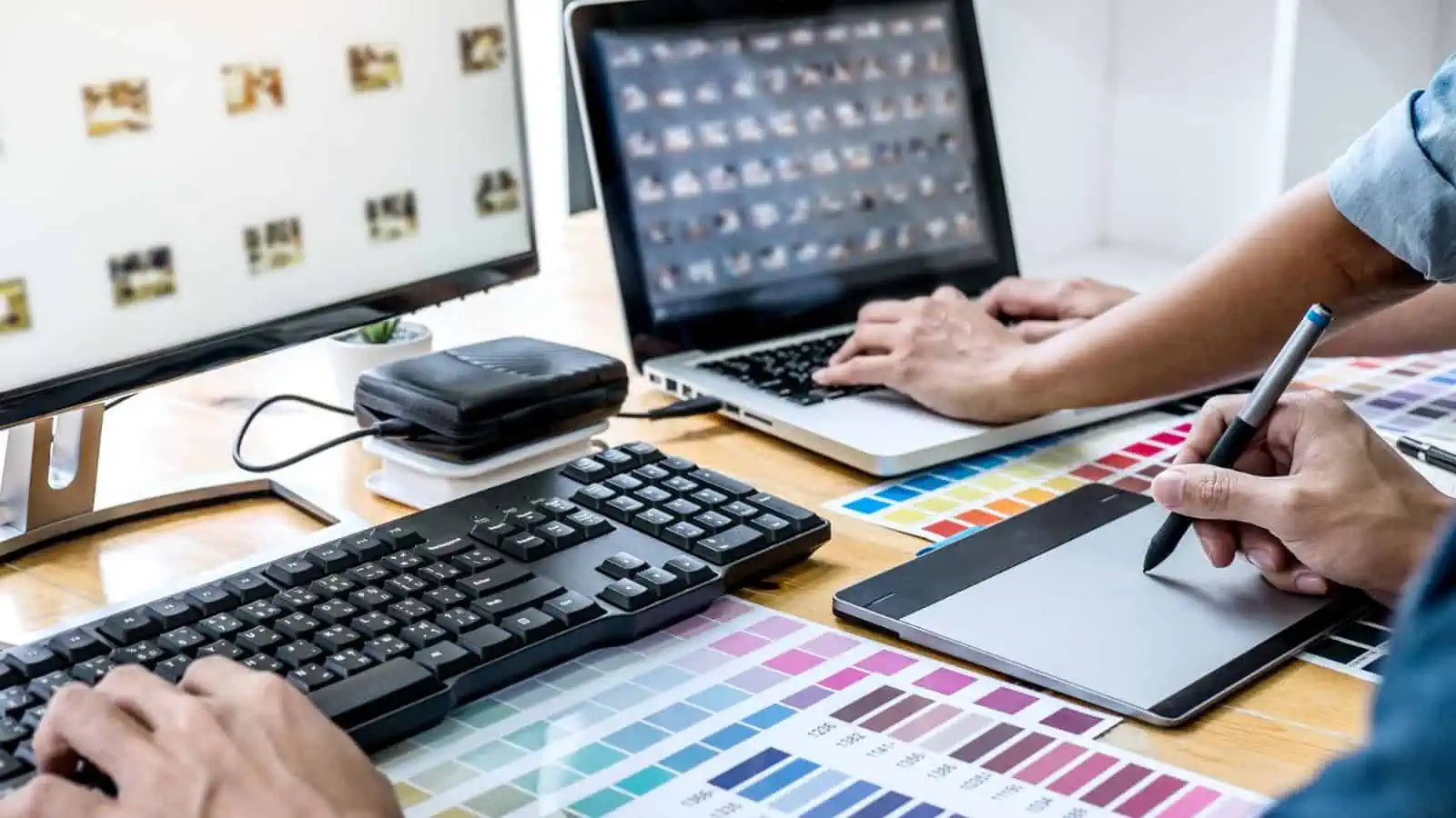 two sets of hands working at desk with color swatches and computers