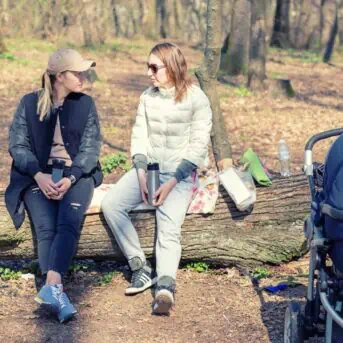 two women sitting on a lot talking next to a baby stroller