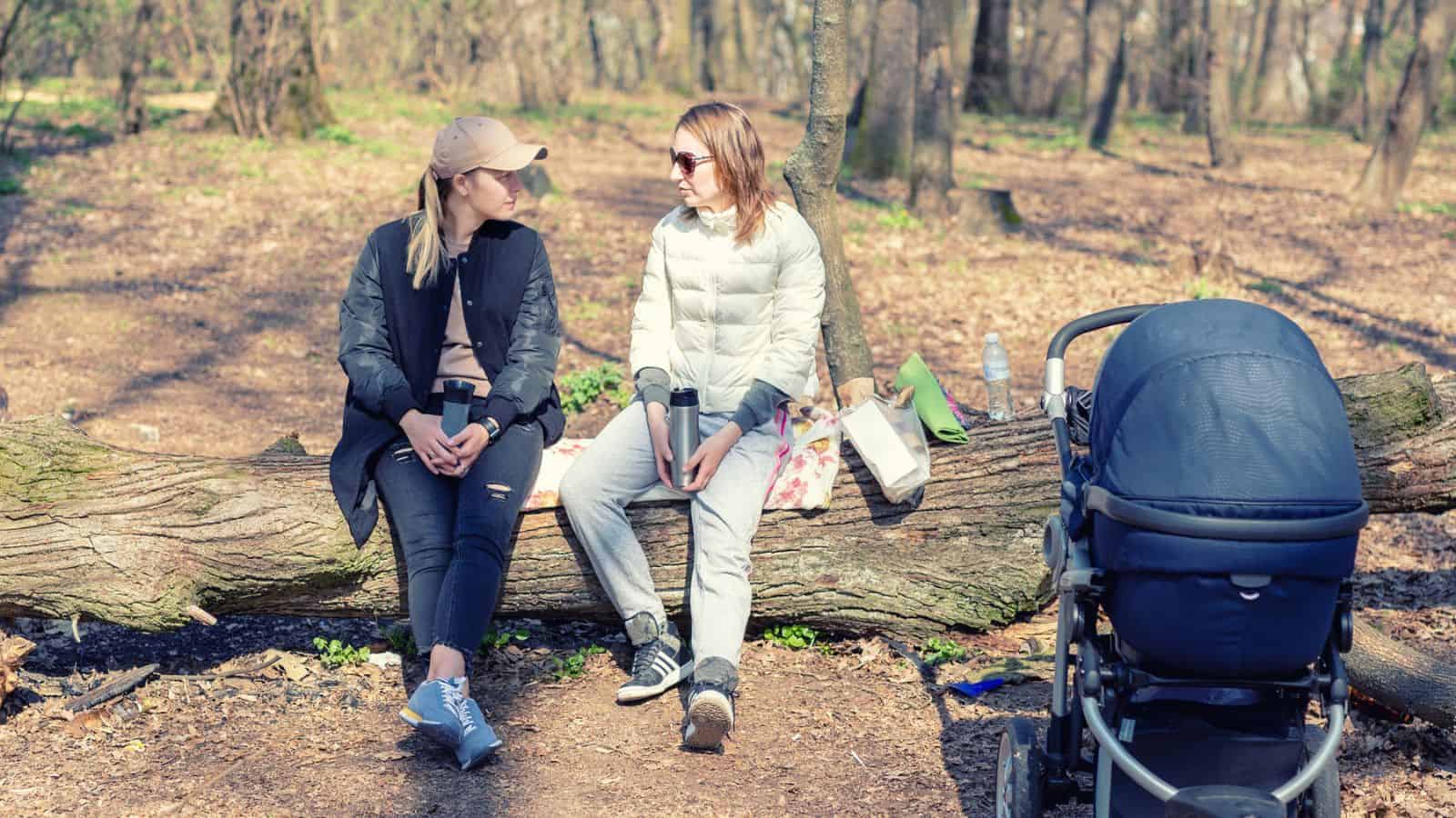 two women sitting on a lot talking next to a baby stroller