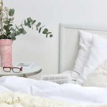 vase and glasses on a nightstand next to a bed