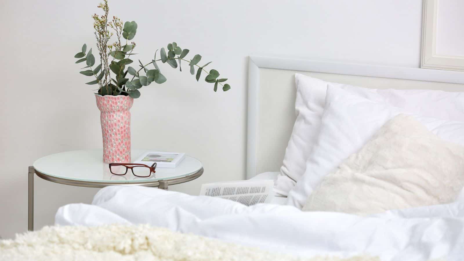 vase and glasses on a nightstand next to a bed