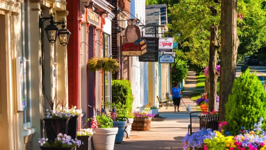 woman walking down small town street full of flowers with her dog