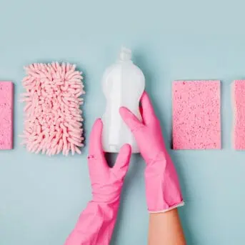 Hands in pink gloves hold detergents and cleaning accessories. Cleaning or housekeeping concept background. Copy space. Flat lay, Top view.