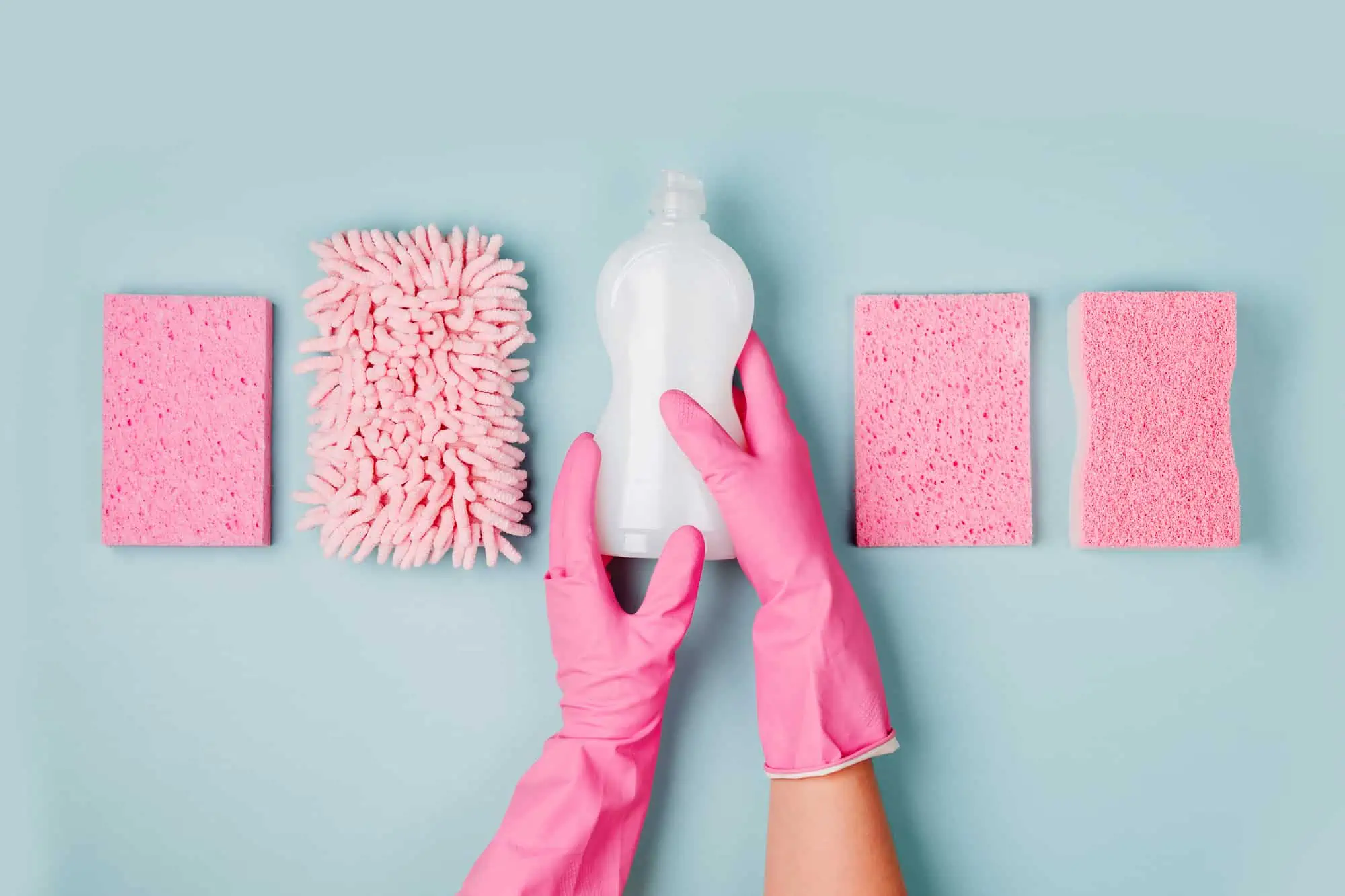 Hands in pink gloves hold detergents and cleaning accessories. Cleaning or housekeeping concept background. Copy space. Flat lay, Top view.