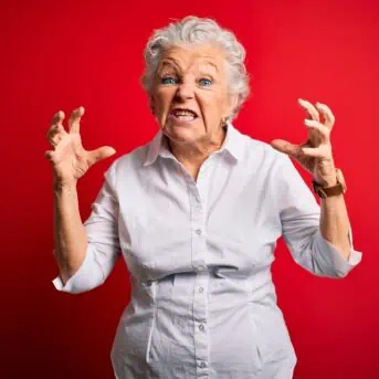 Senior beautiful woman wearing elegant shirt standing over isolated red background Shouting frustrated with rage, hands trying to strangle, yelling mad