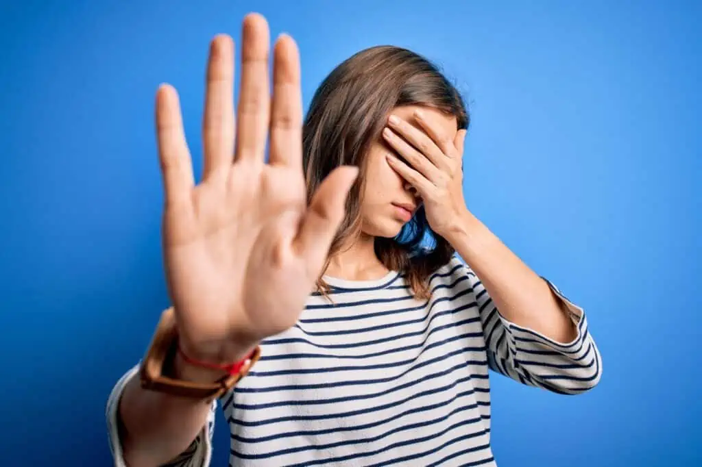 Young beautiful blonde girl wearing casual sweater standing over blue isolated background covering eyes with hands and doing stop gesture with sad and fear expression. Embarrassed and negative concept.