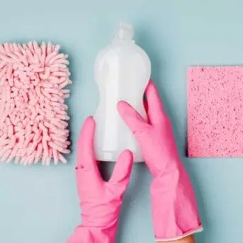 Hands in pink gloves hold detergents and cleaning accessories. Cleaning or housekeeping concept background. Copy space. Flat lay, Top view.