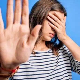 Young beautiful blonde girl wearing casual sweater standing over blue isolated background covering eyes with hands and doing stop gesture with sad and fear expression. Embarrassed and negative concept.