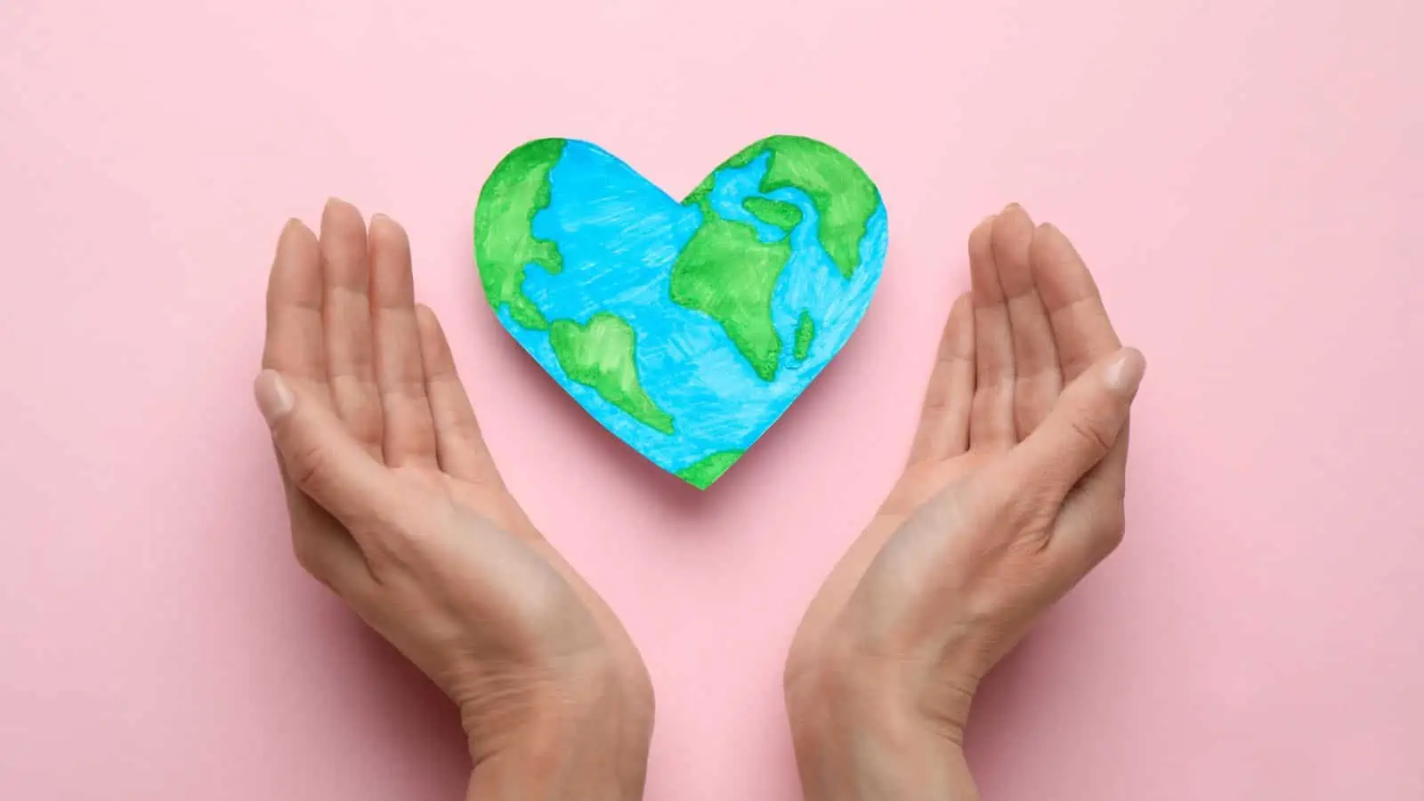 hands surrounding heart image of earth pink background