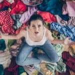 upset woman sitting on and surrounded by clothes