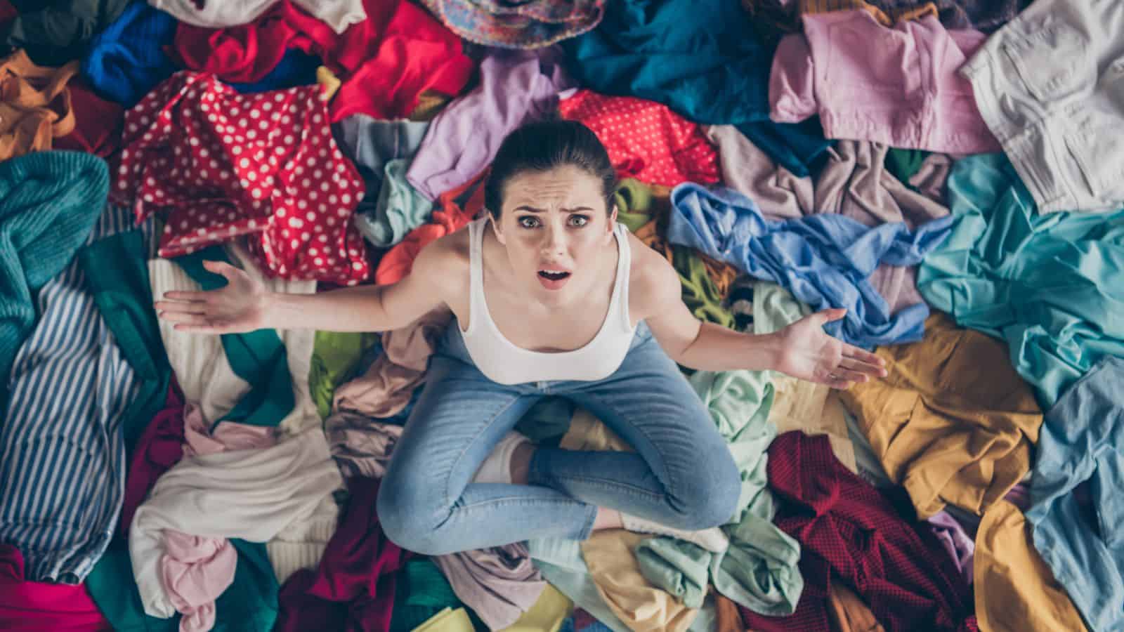 upset woman sitting on and surrounded by clothes