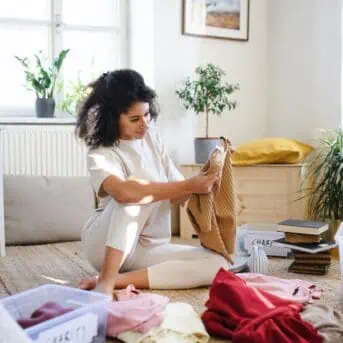 woman sitting on floor sorting and decluttering clothes