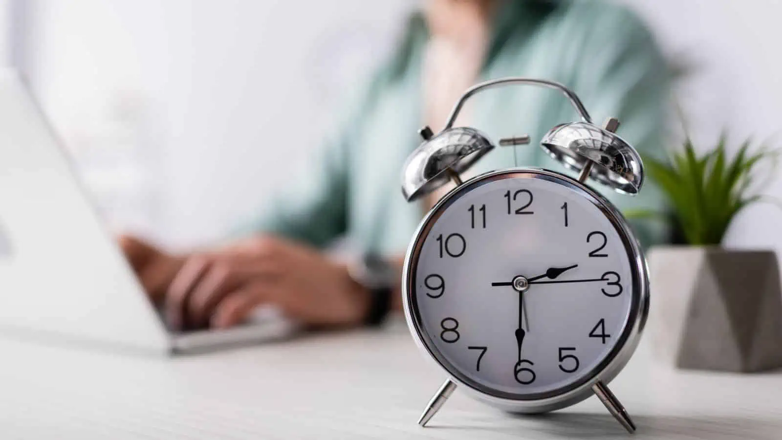 old fashioned alarm clock on desk with woman working on computer in background