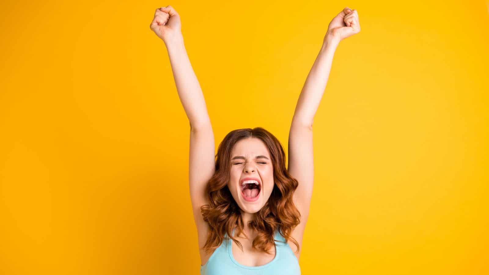 woman celebrating with arms in air yellow background