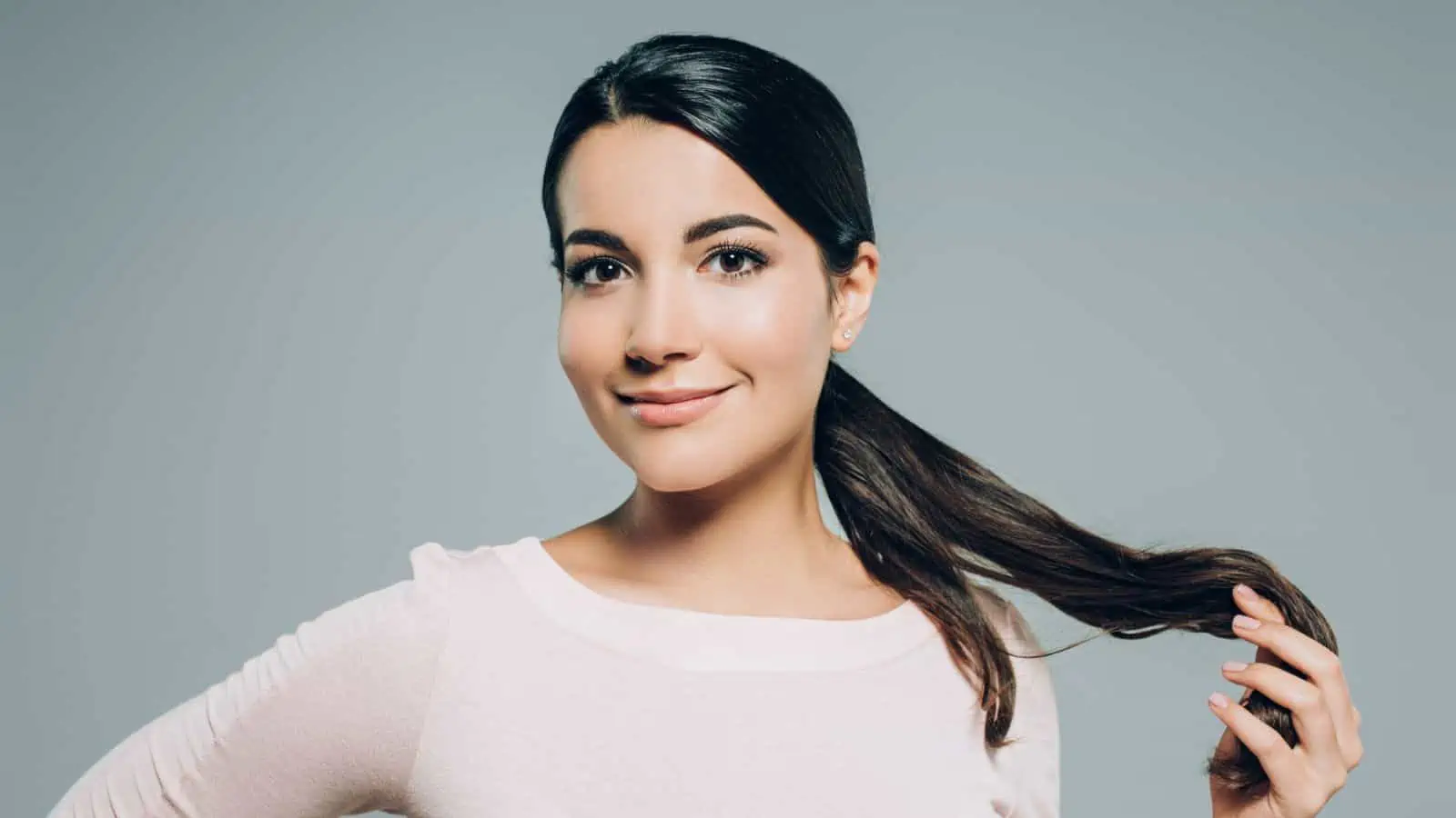 woman smiling and touching her own hair in ponytail