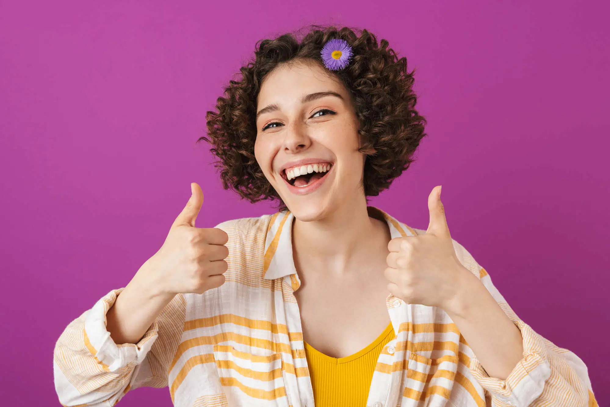 Portrait of an attractive happy young woman with curly brunette hair standing isolated over violet background, thumbs up