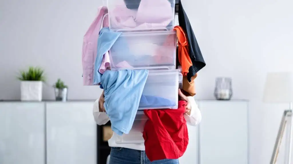 person holding plastic containers overflowing with clothes