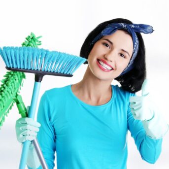 smiling woman giving thumbs up and holding a mop and broom