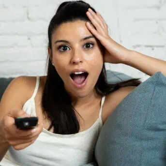 woman sitting on couch with mouth open and remote control in hand