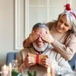 Woman covering man's eyes holding Christmas gift (1)