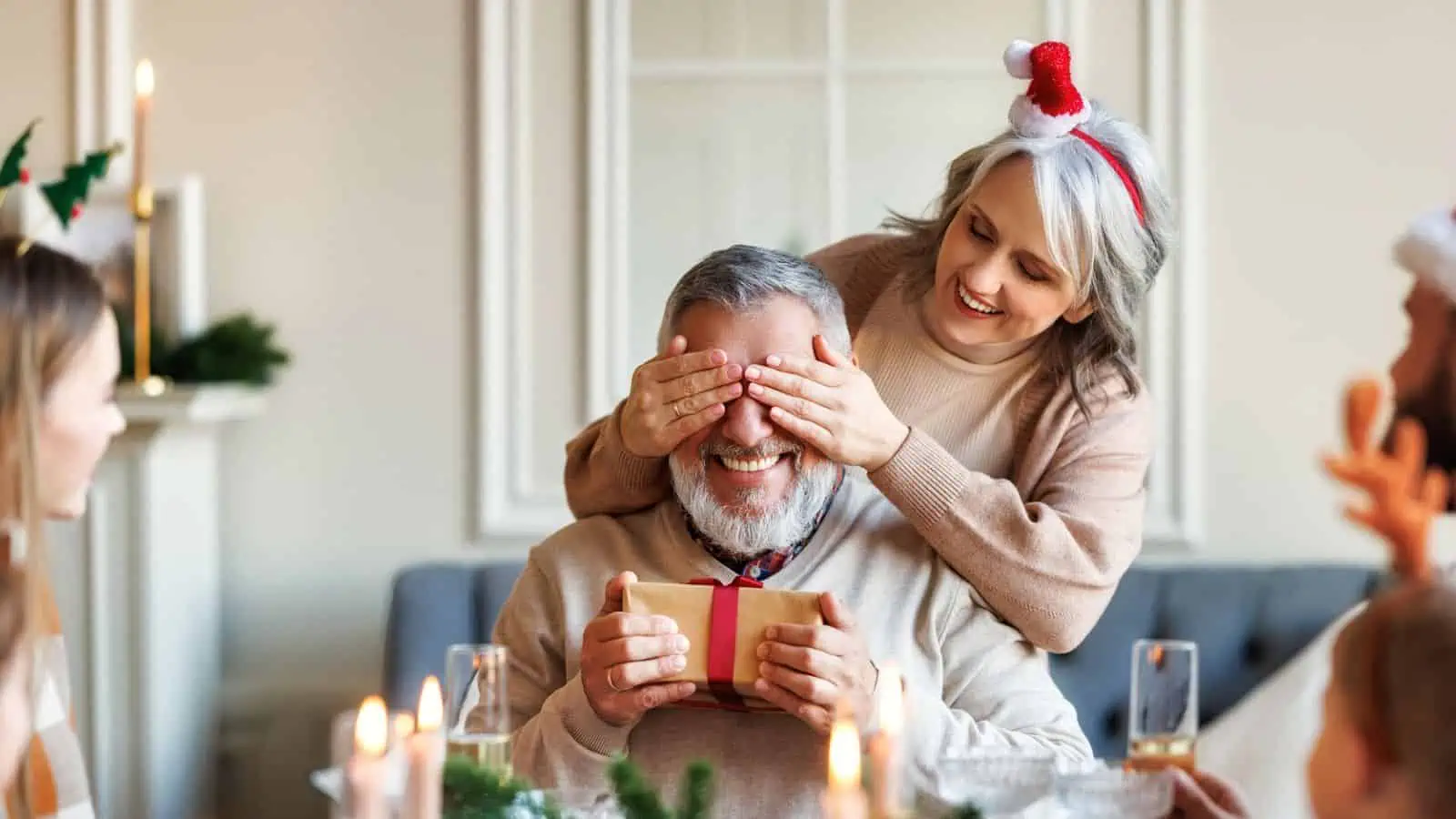 Woman covering man's eyes holding Christmas gift (1)