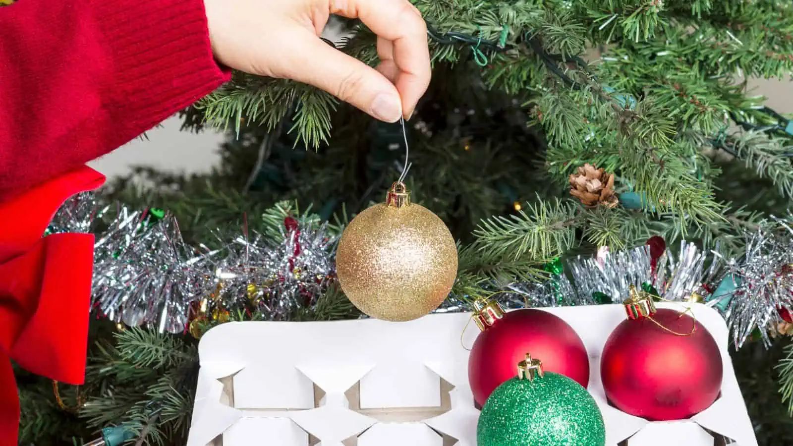 putting Christmas ornaments in organizer in front of a Christmas tree