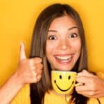 excited woman holding a smiley face mug and giving a thumbs up