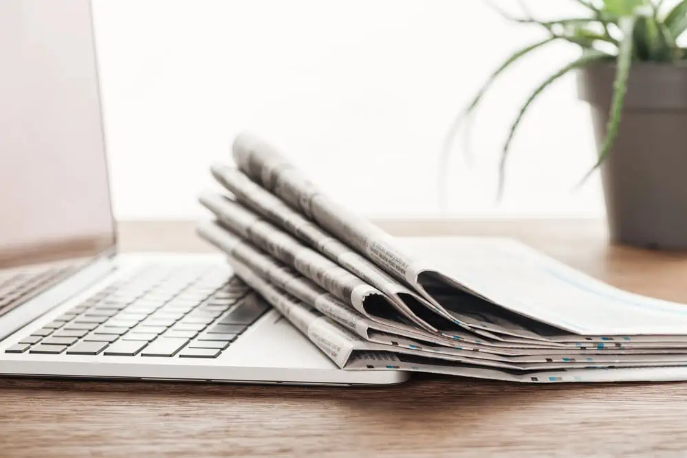 newspapers on desk with computer and plant