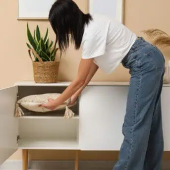 Woman putting pillow in chest of drawers in room